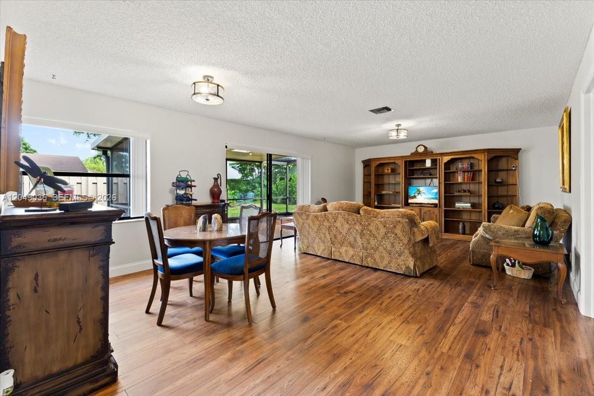 A living and dining room area features wood-look flooring, a large wall unit, and furniture — 901 NW 26th Ave, Delray Beach FL 33445, DELRAY BEACH, FL