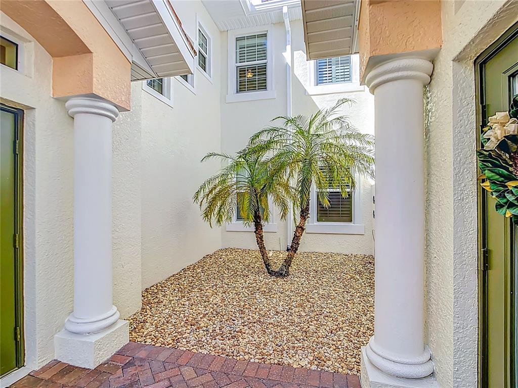 A small courtyard features a palm tree, gravel ground, and two white columns — 198 BELLA VISTA TERRACE UNIT C, NORTH VENICE, FL