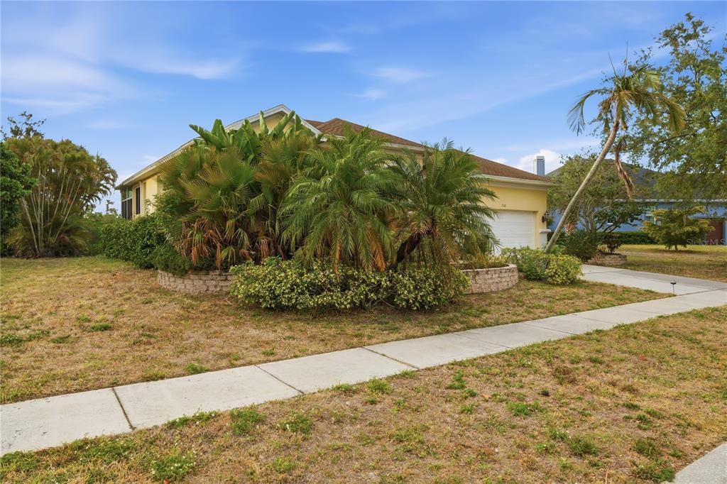 A single-story house with a yellow exterior, a two-car garage, and dense landscaping in front — 718 BUNKER VIEW DRIVE, APOLLO BEACH, FL