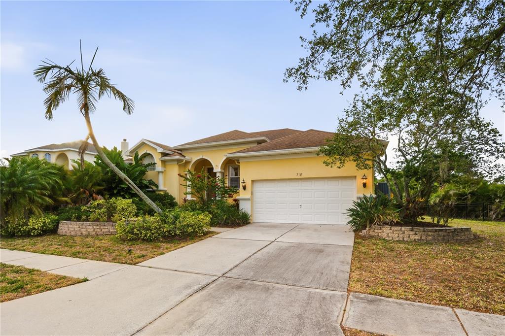 A yellow single-story house with a two-car garage and a palm tree in the front — 718 BUNKER VIEW DRIVE, APOLLO BEACH, FL