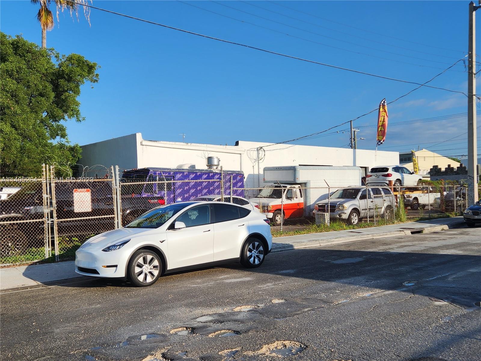 A white Tesla is parked on a street in front of a fenced-in commercial lot — 60 NW 20th St, Miami FL 33127, MIAMI, FL