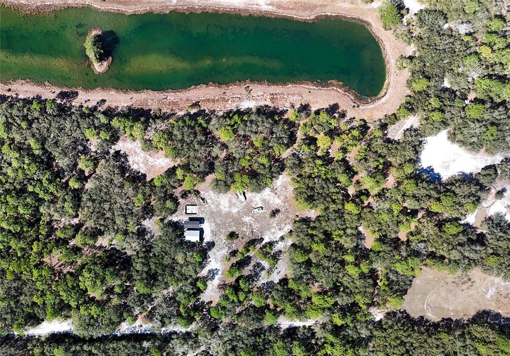An aerial view shows a small house situated in a wooded area near a pond — 251 AMBER TRAIL, PALM COAST, FL