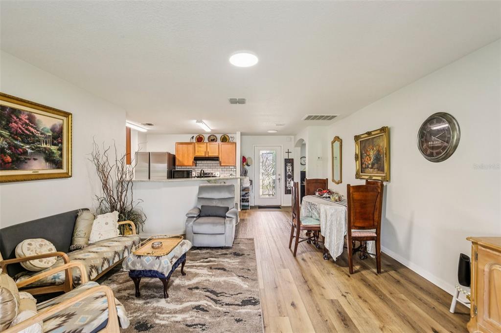 An open-concept living and dining area features wood-look flooring, a kitchen counter, and neutral walls — 636 CHATHAM WALK DRIVE, RUSKIN, FL
