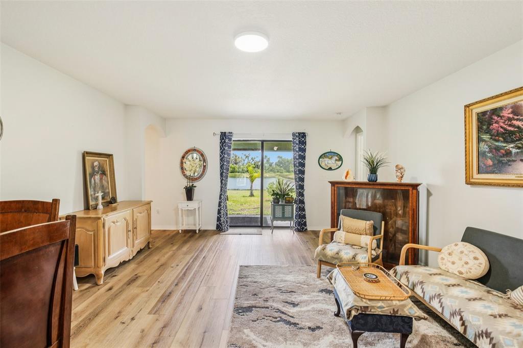 A living room with wood-look flooring, a sliding glass door, and a view of water — 636 CHATHAM WALK DRIVE, RUSKIN, FL