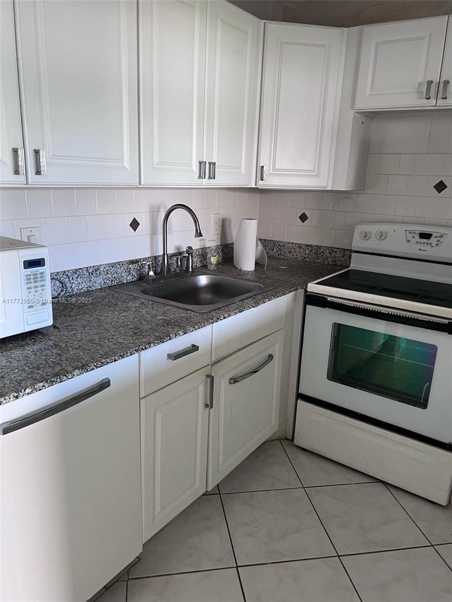 A kitchen features white cabinets, granite countertops, a stainless steel sink, and a white stove — 90 Fanshaw C # 90, Boca Raton FL 33434, BOCA RATON, FL