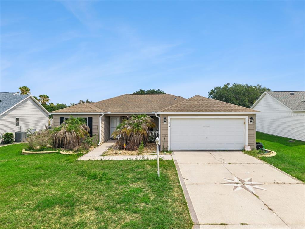 A single-story house with tan siding, a two-car garage, and a front lawn — 1575 HOLLYBERRY PLACE, THE VILLAGES, FL