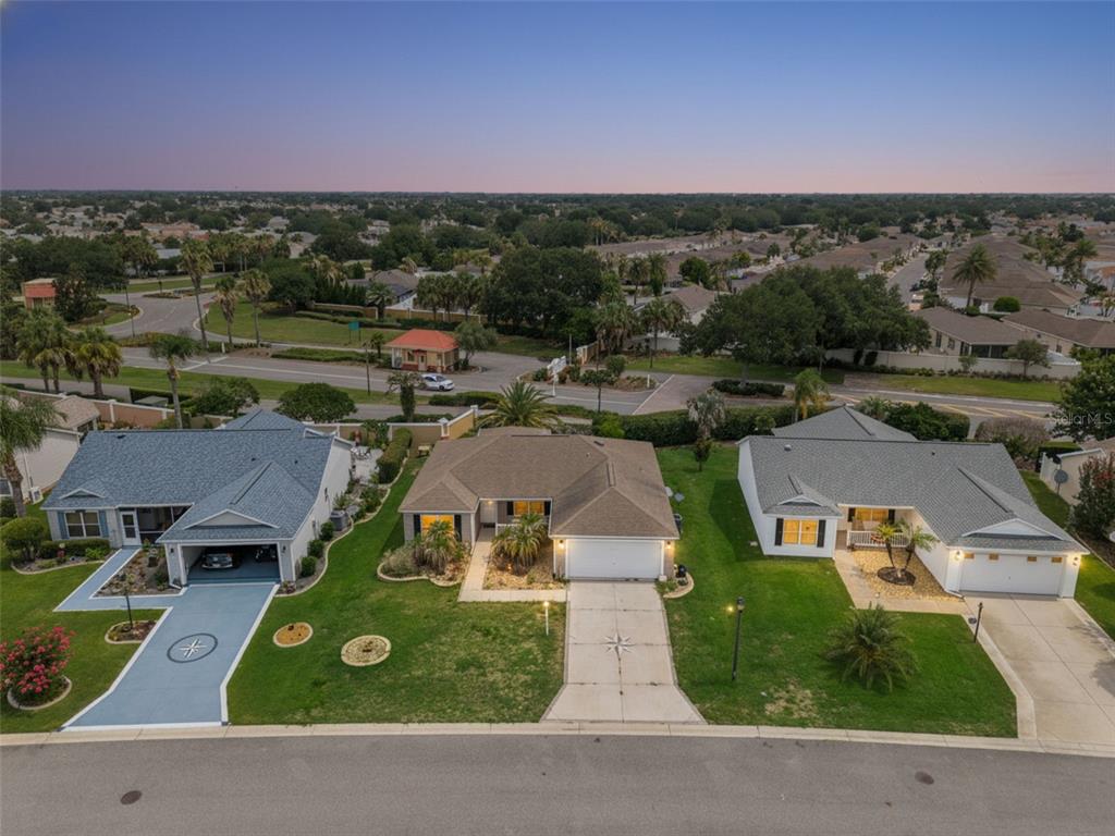 An aerial view shows three suburban houses with driveways and lawns along a curved street — 1575 HOLLYBERRY PLACE, THE VILLAGES, FL