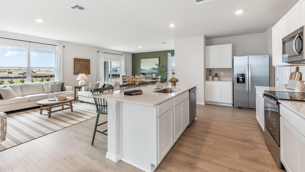 An open-concept kitchen and living area featuring white cabinetry, stainless steel appliances, and wood flooring — 9952 MORNING MEADOWLARK TRAIL, PARRISH, FL