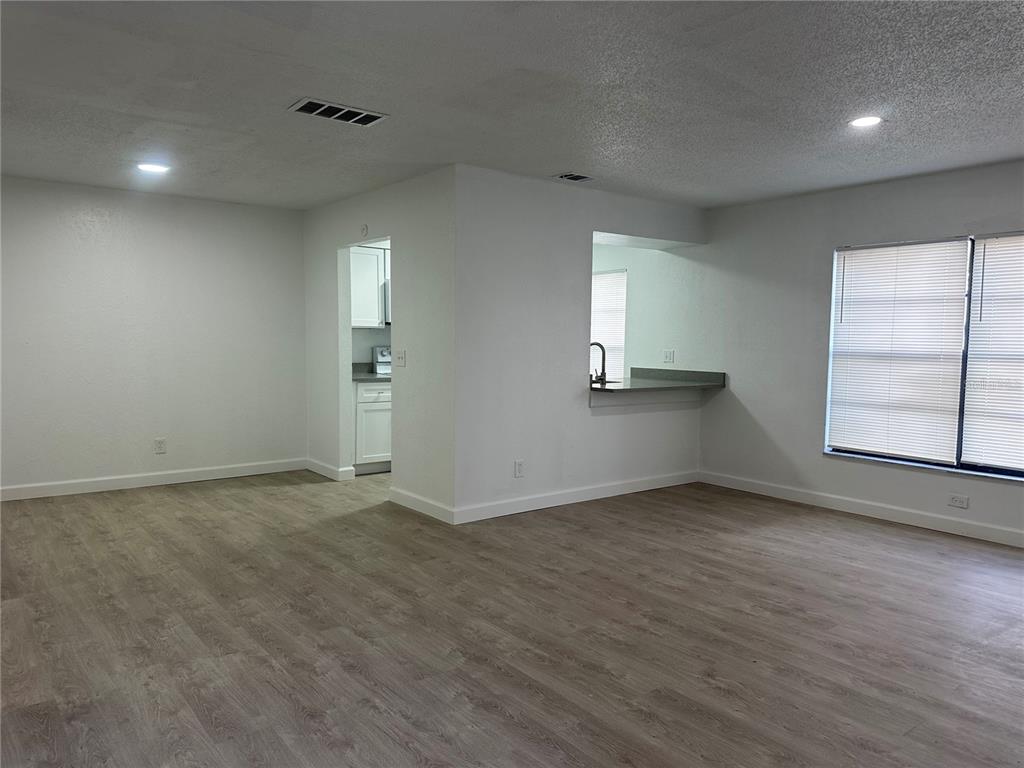 An open-concept living area features light wood-look flooring, white walls, and a kitchen pass-through window — 8432 CAMDEN STREET UNIT A, TAMPA, FL