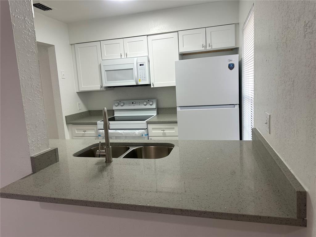 A kitchen features white cabinets, a white refrigerator, a microwave, and gray speckled countertops — 8432 CAMDEN STREET UNIT A, TAMPA, FL