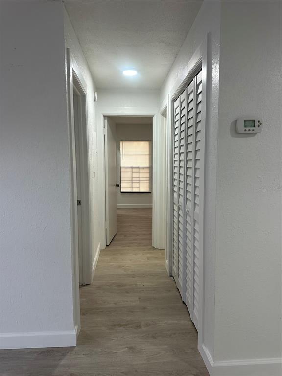 A hallway with light wood-look flooring, white walls, louvered closet doors, and a thermostat — 8432 CAMDEN STREET UNIT A, TAMPA, FL