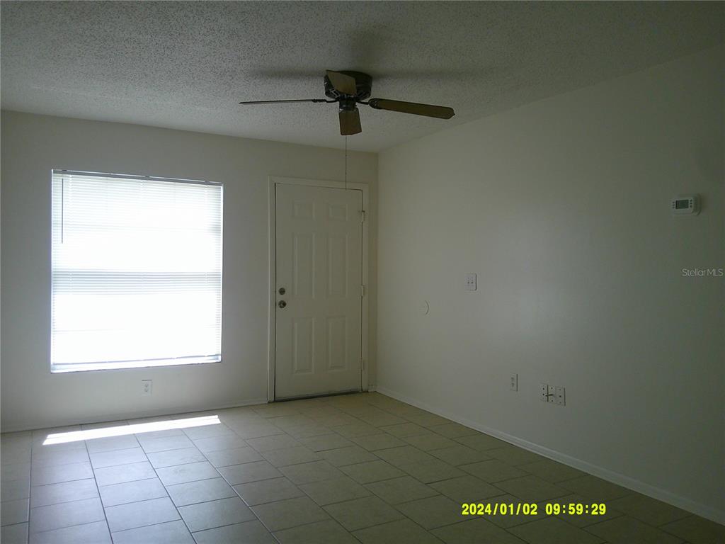 An empty room with light-colored tile flooring, a ceiling fan, and a white entry door — 71 LAKE VILLA WAY, KISSIMMEE, FL
