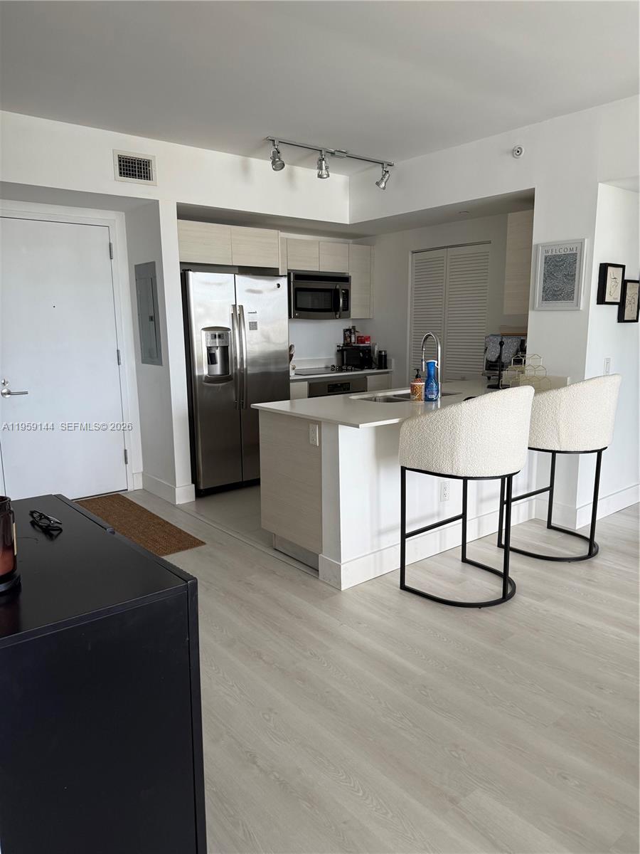 A modern kitchen features light wood cabinetry, stainless steel appliances, and a white breakfast bar — 4250 Biscayne Blvd # 1618, Miami FL 33137, MIAMI, FL
