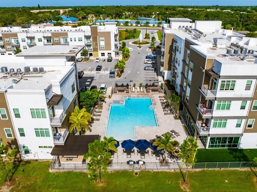 An aerial view of an apartment complex swimming pool surrounded by lounge chairs and buildings — 1185 S PINELLAS AVENUE UNIT A2, TARPON SPRINGS, FL