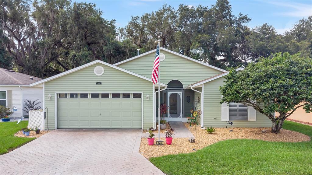 A light green single-story house with a two-car garage and a paved driveway — 842 OLD OAKS LANE, LEESBURG, FL