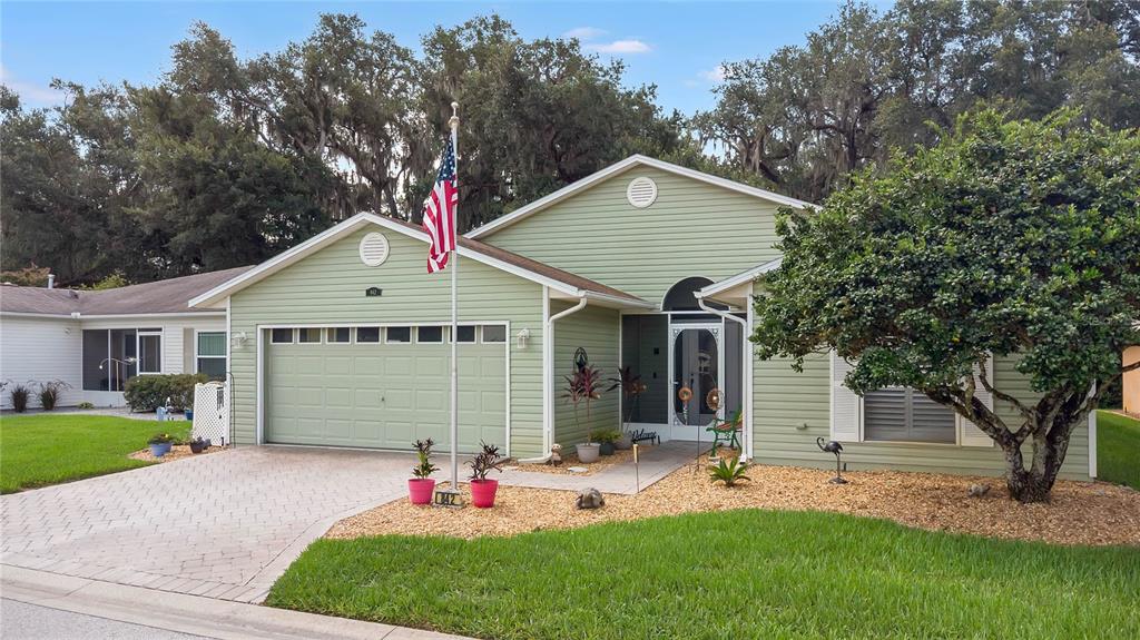 A light green single-story house with a two-car garage, a flag pole, and landscaped yard — 842 OLD OAKS LANE, LEESBURG, FL