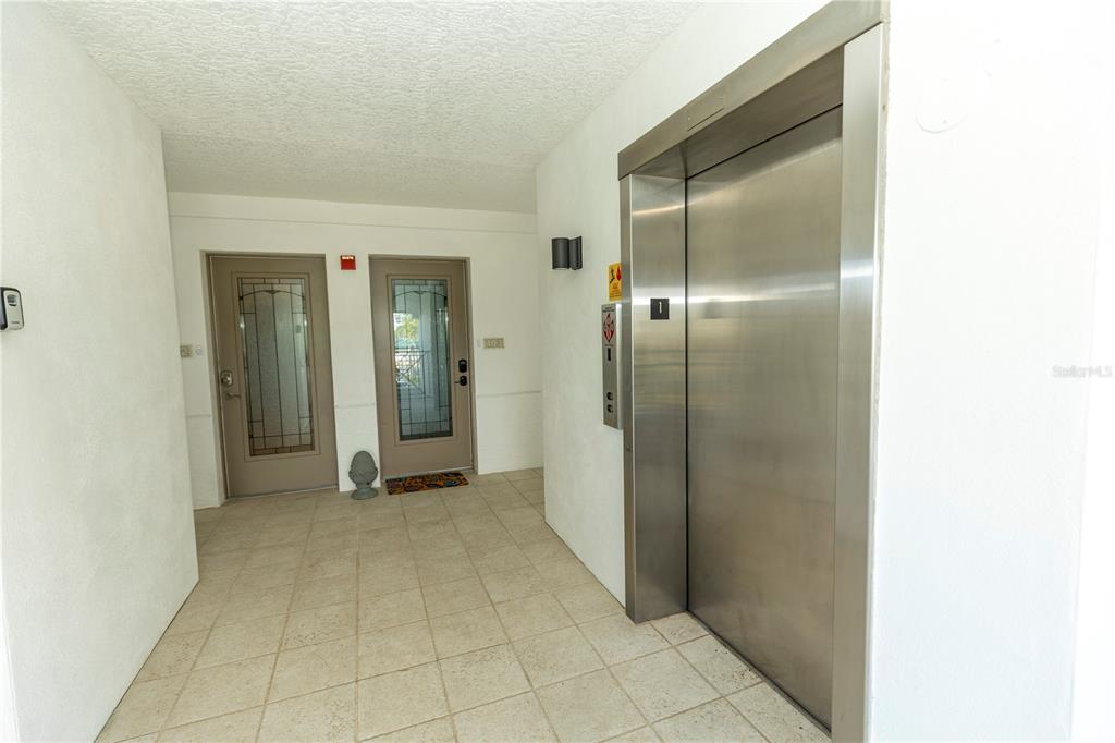 A hallway features a tiled floor, two glass-paneled doors, and a stainless steel elevator — 9203 GRIGGS ROAD UNIT 102, ENGLEWOOD, FL