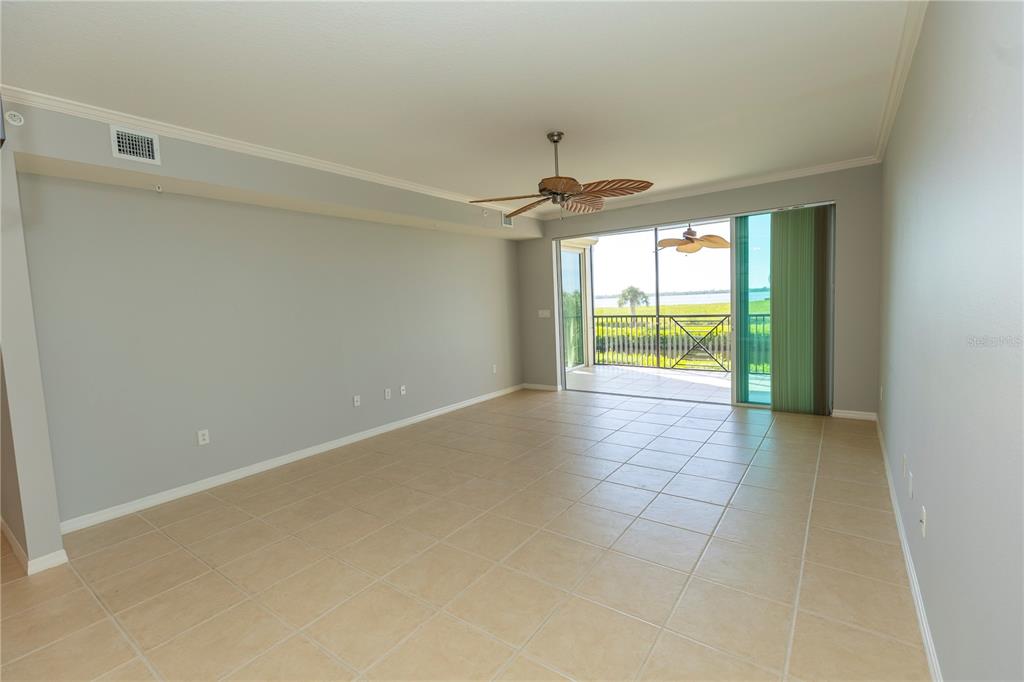 An empty living room with tile flooring, a ceiling fan, and a sliding glass door — 9203 GRIGGS ROAD UNIT 102, ENGLEWOOD, FL