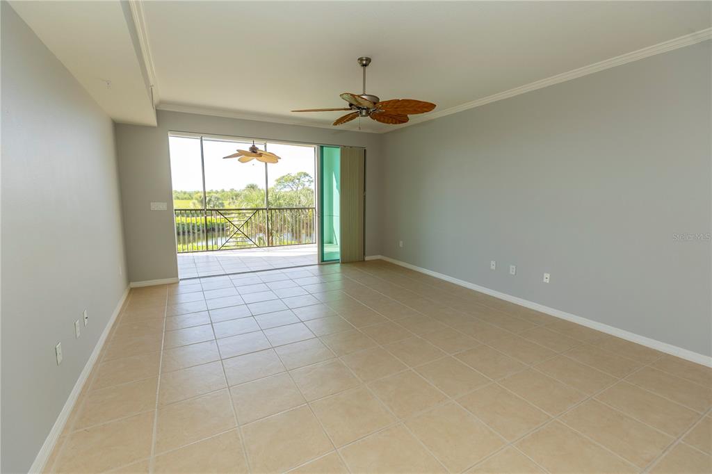An empty living room with light tile flooring, gray walls, a ceiling fan, and a balcony — 9203 GRIGGS ROAD UNIT 102, ENGLEWOOD, FL