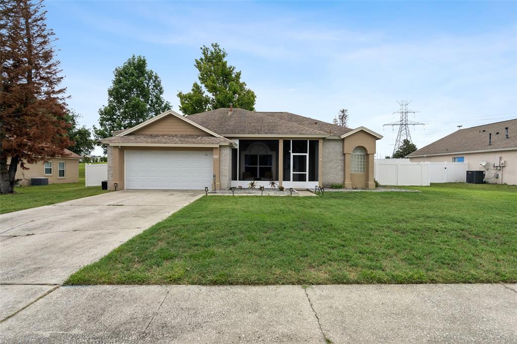 A single-story house with a two-car garage, a screened front porch, and a grassy lawn — 14825 GREATER PINES BOULEVARD, CLERMONT, FL