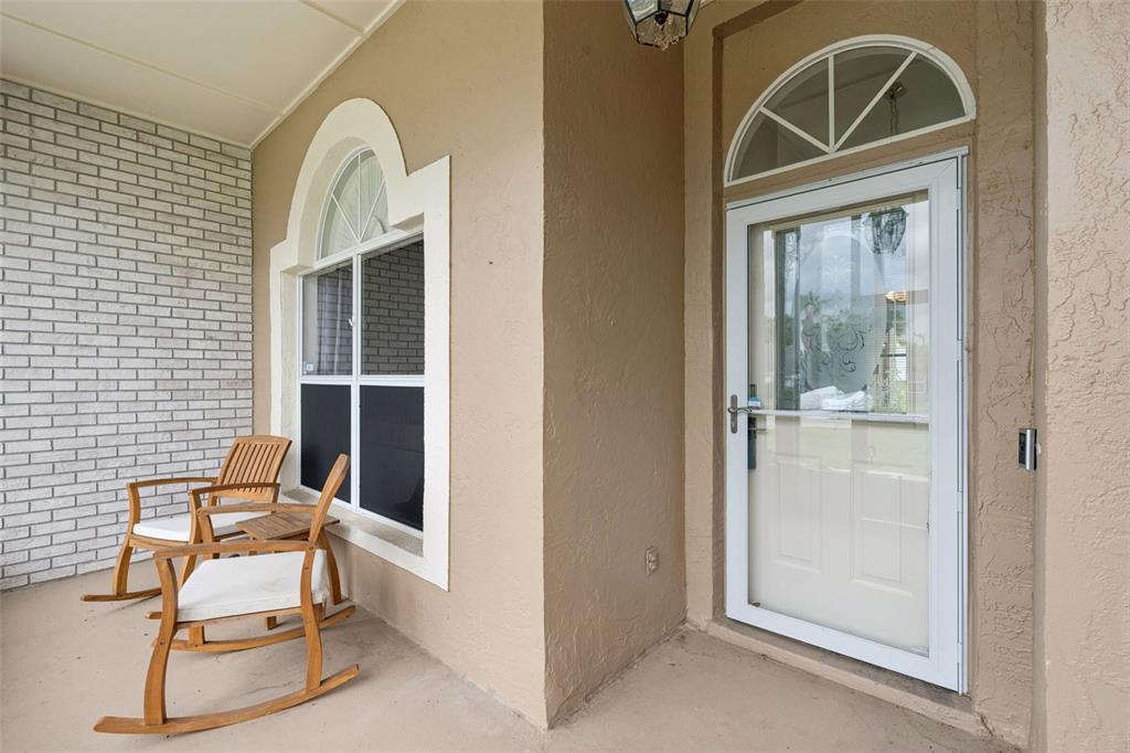 A covered porch features a white-framed glass door, a window with a decorative arch, and two rocking chairs — 14825 GREATER PINES BOULEVARD, CLERMONT, FL