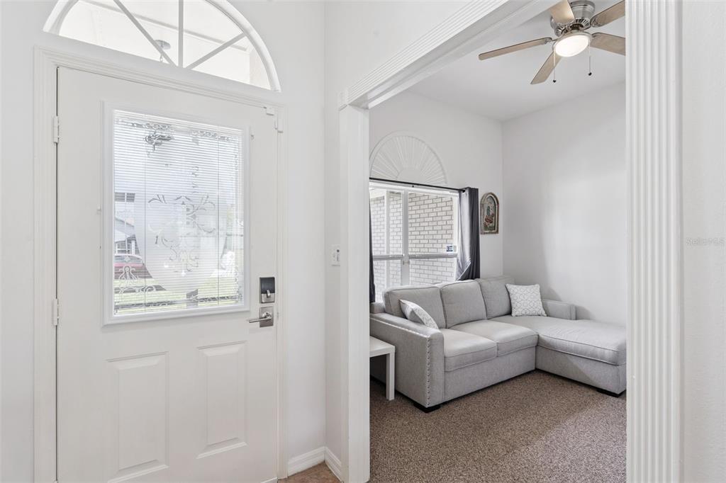A white front door opens into a carpeted room featuring a gray sectional sofa — 14825 GREATER PINES BOULEVARD, CLERMONT, FL