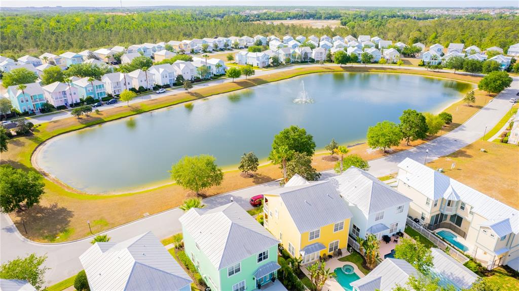 An aerial view shows a residential neighborhood with colorful houses surrounding a central pond — 1545 FAIRVIEW CIRCLE, REUNION, FL