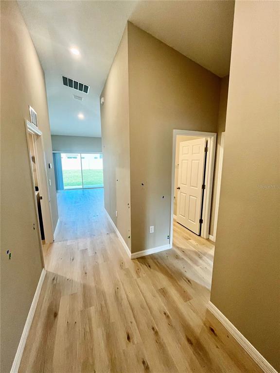 A hallway with light wood flooring leads toward a living area with a sliding glass door — 14664 GALLOP RUN DRIVE, LITHIA, FL