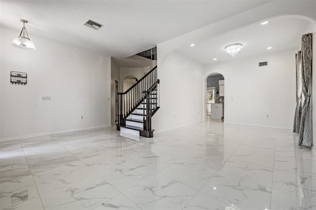 A bright, open-concept living area features white marble-look tile floors and a dark wood staircase — 380 ROSALIND LANE, OLDSMAR, FL