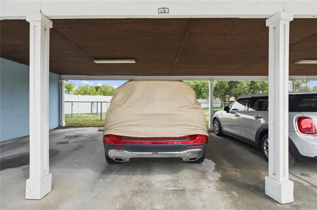 A covered parking space contains a car under a tan cover and a silver vehicle — 151 SEAHORSE DRIVE SE UNIT B, ST PETERSBURG, FL