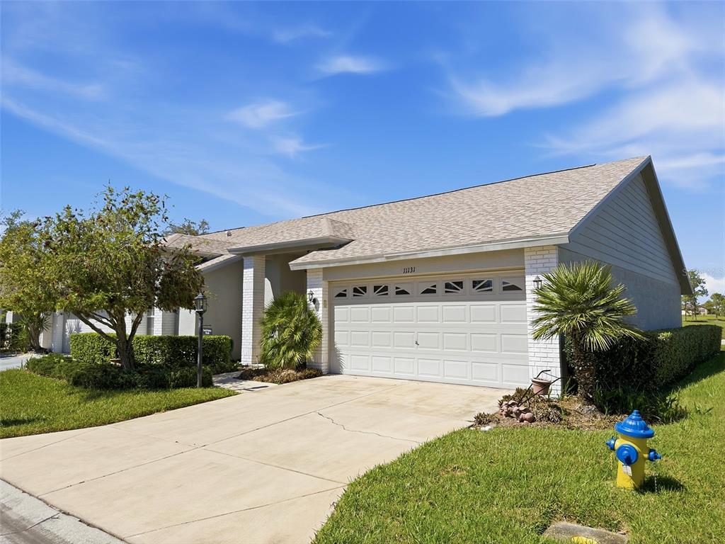 A single-story house with a beige garage, white brick accents, and a fire hydrant nearby — 11131 HOLLANDER AVENUE, HUDSON, FL