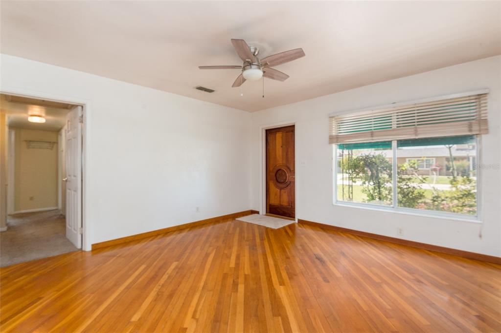 An empty room features hardwood floors, a ceiling fan, a wooden door, and a large window — 4425 W BAY VILLA AVENUE, TAMPA, FL