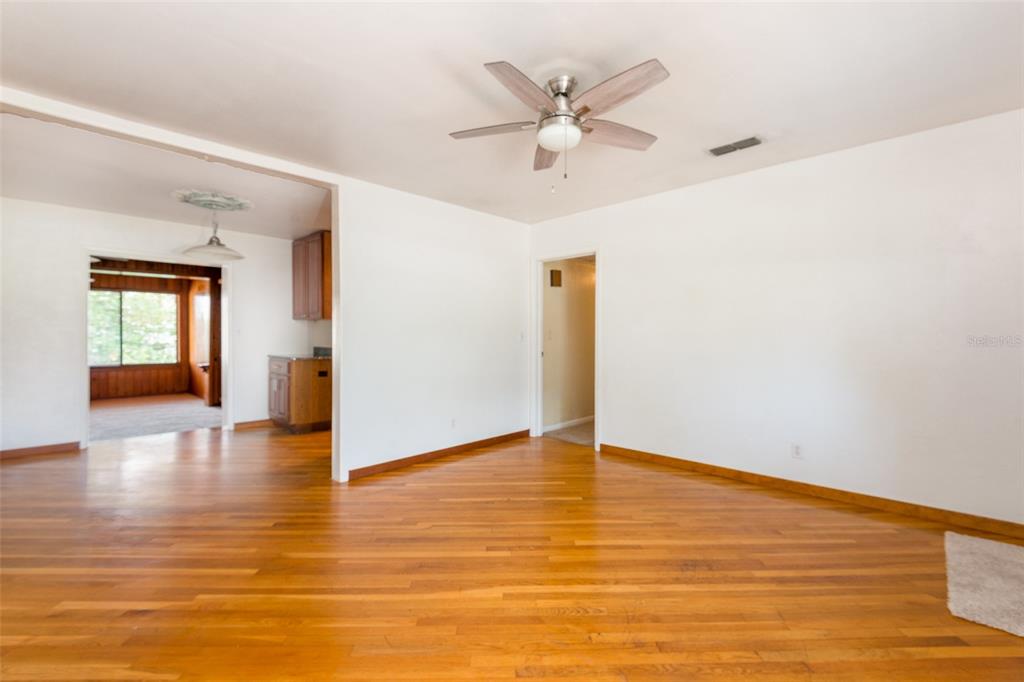 An empty room with hardwood floors, a ceiling fan, and an adjacent kitchen area — 4425 W BAY VILLA AVENUE, TAMPA, FL