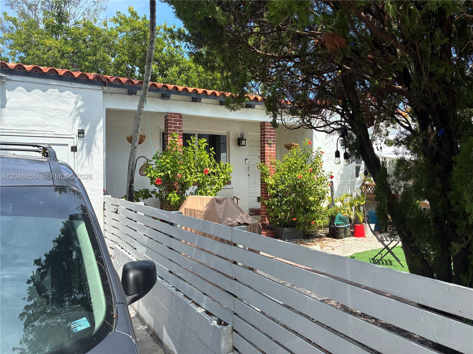A white house with a red tile roof features a front porch and wooden fence — 7929 Abbott Ave, Miami Beach FL 33141, MIAMI BEACH, FL
