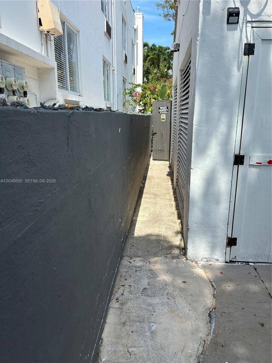 A narrow concrete walkway sits between a dark gray wall and a white building exterior — 7929 Abbott Ave, Miami Beach FL 33141, MIAMI BEACH, FL