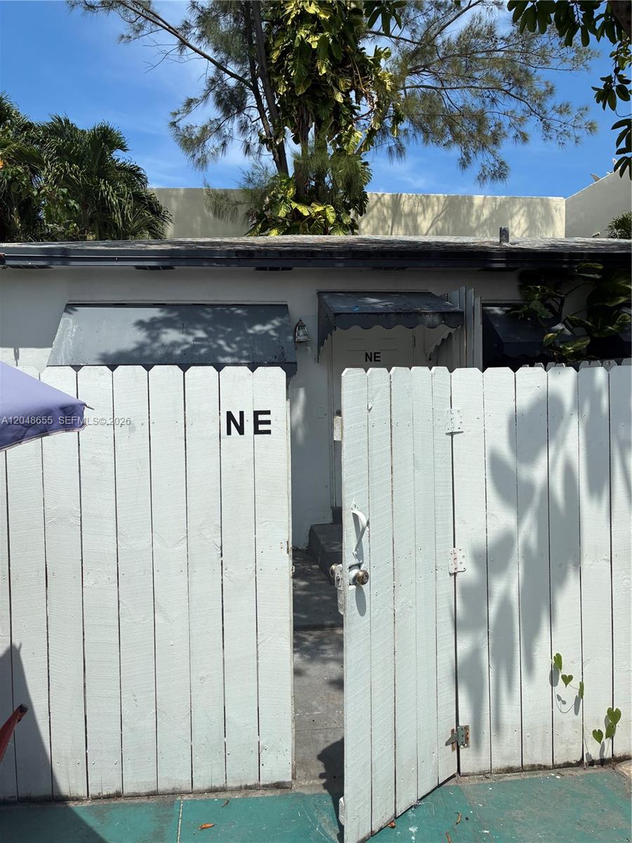 A white wooden fence with an open gate leads to the entrance of a building — 7929 Abbott Ave, Miami Beach FL 33141, MIAMI BEACH, FL
