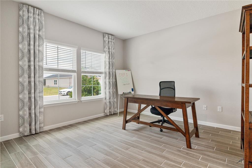 A home office features wood-look tile flooring, a wooden desk, and two windows with curtains — 9324 SW 58TH CIRCLE, OCALA, FL