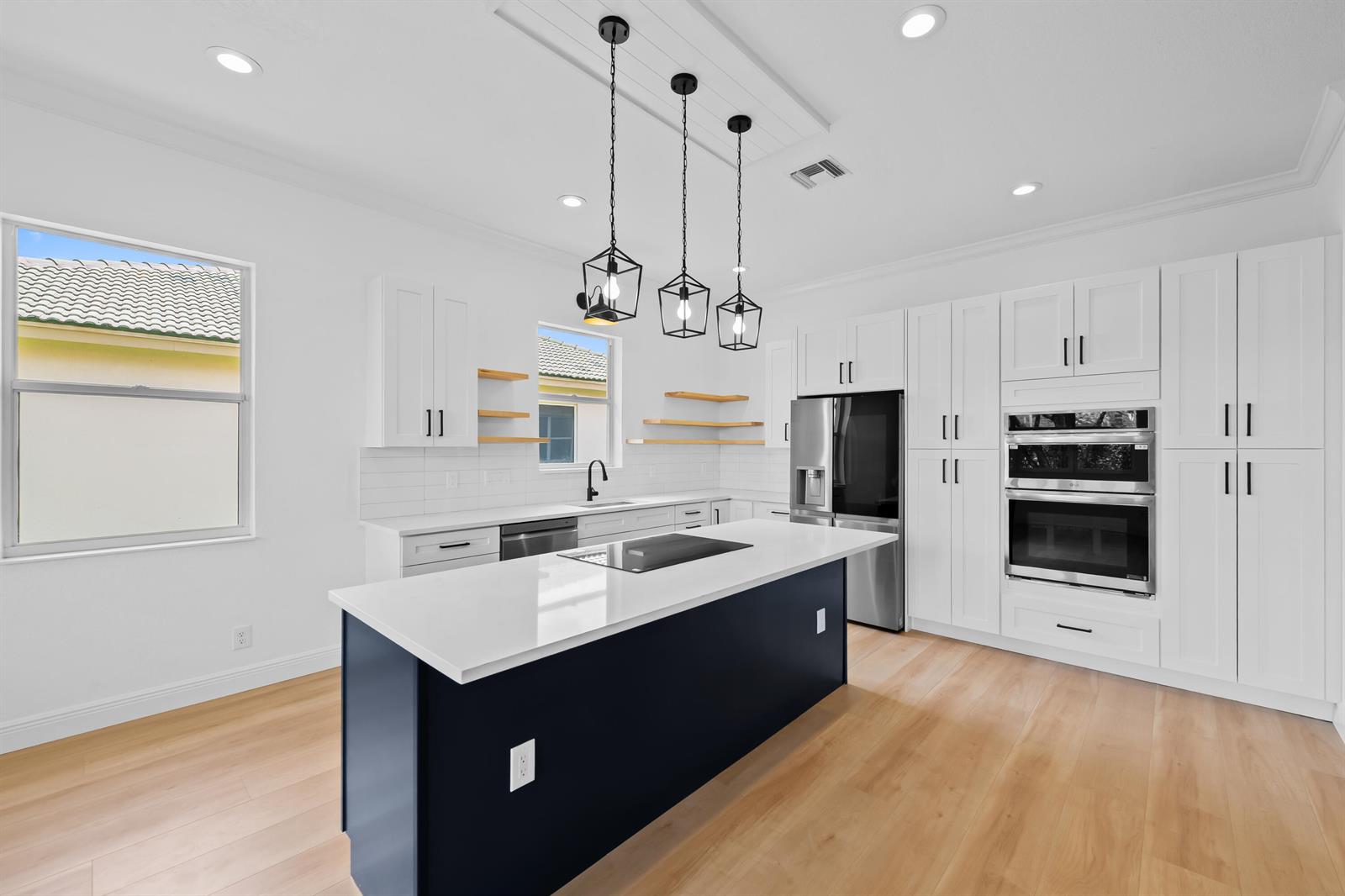 A modern kitchen features white cabinetry, a dark blue island, and light wood flooring — 8245 Marsala Way, Boynton Beach FL 33472, BOYNTON BEACH, FL