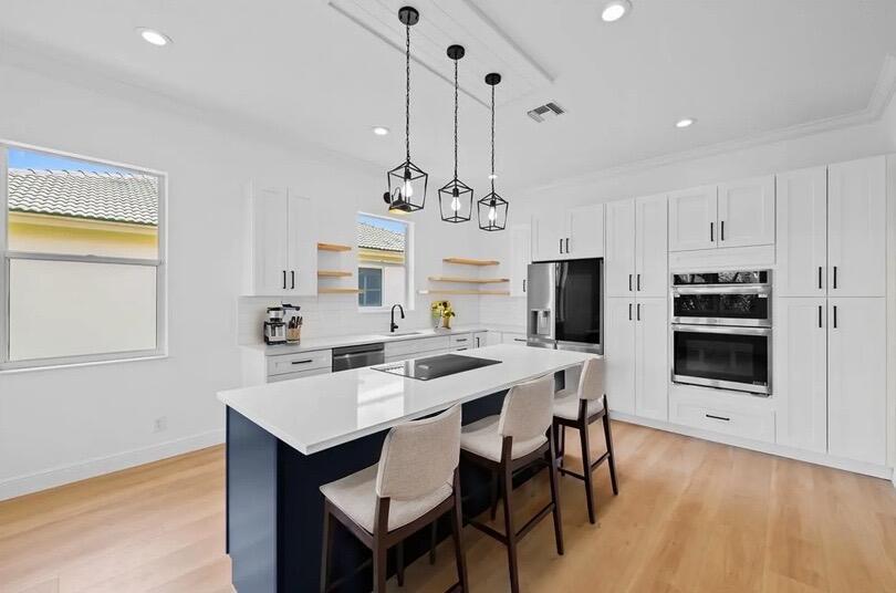 A modern kitchen features white cabinetry, a dark blue island, and light wood flooring — 8245 Marsala Way, Boynton Beach FL 33472, BOYNTON BEACH, FL