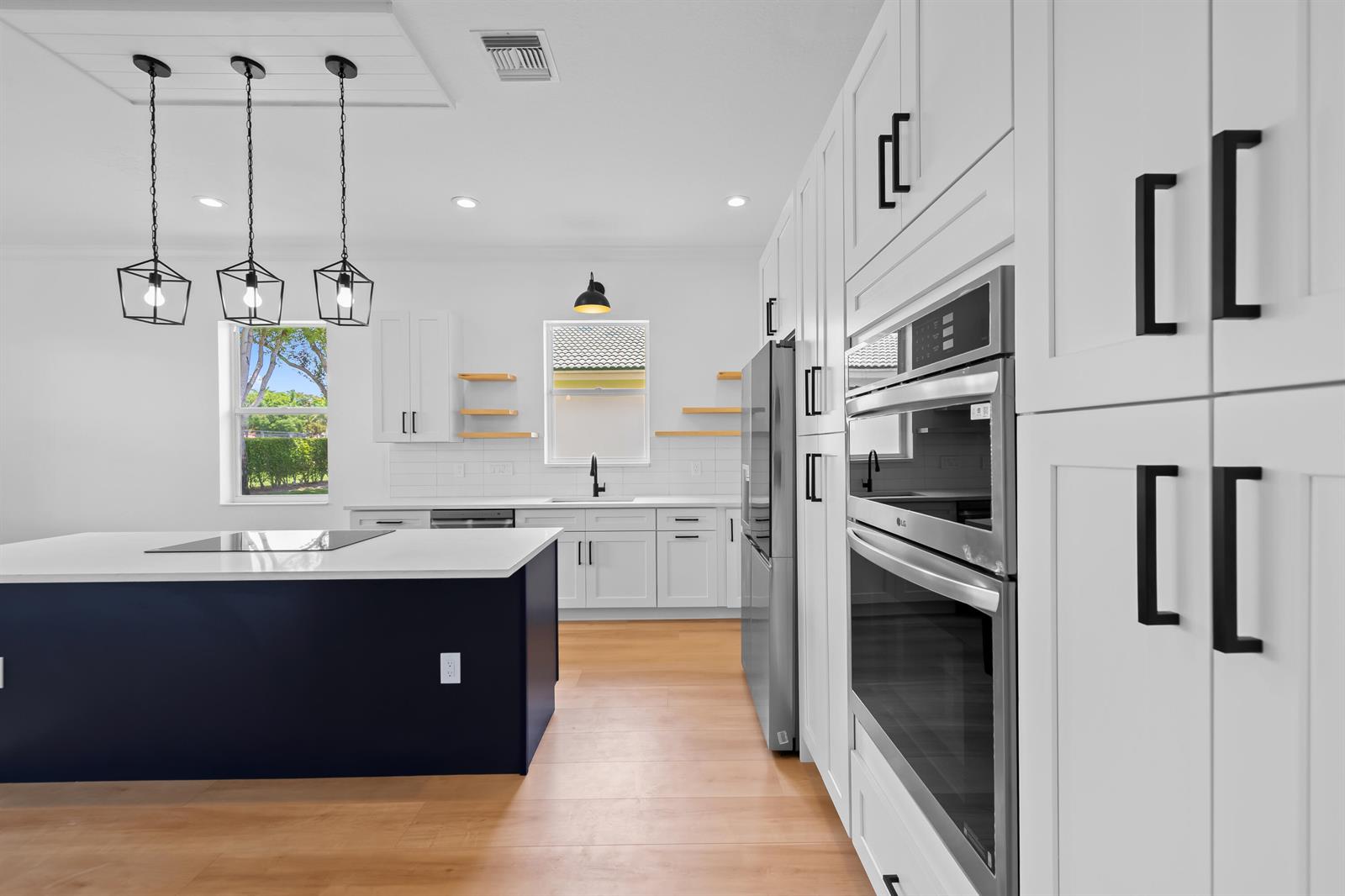 A modern kitchen features white cabinetry, a dark blue island, and stainless steel appliances — 8245 Marsala Way, Boynton Beach FL 33472, BOYNTON BEACH, FL
