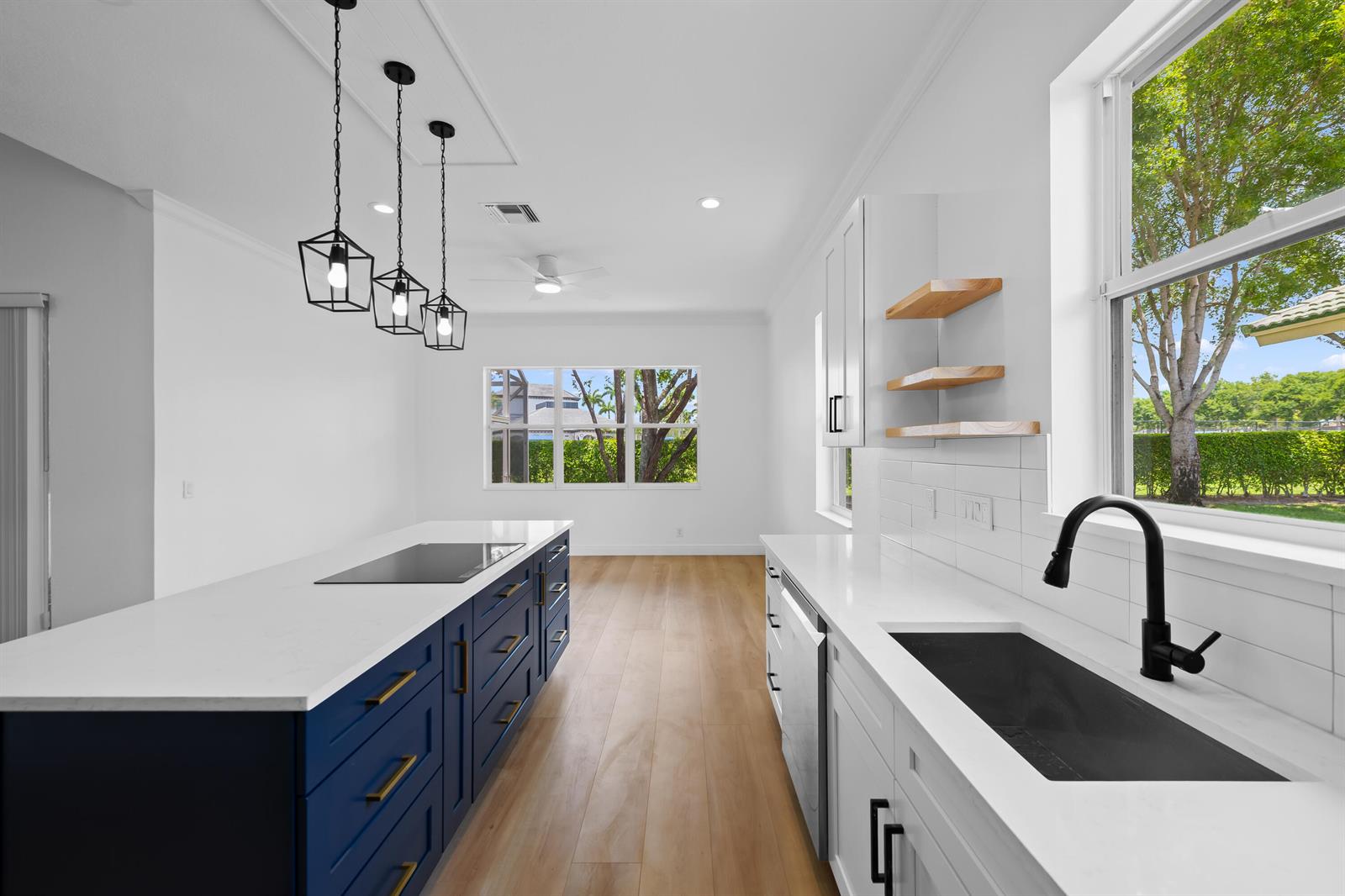 A modern kitchen features a blue island, white cabinets, light wood floors, and pendant lighting — 8245 Marsala Way, Boynton Beach FL 33472, BOYNTON BEACH, FL