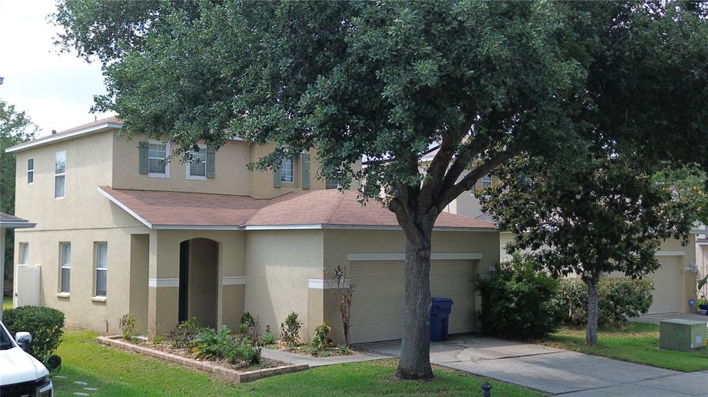 A two-story tan stucco house with a brown shingled roof and a front-facing garage — 9631 SIMEON DRIVE, LAND O LAKES, FL