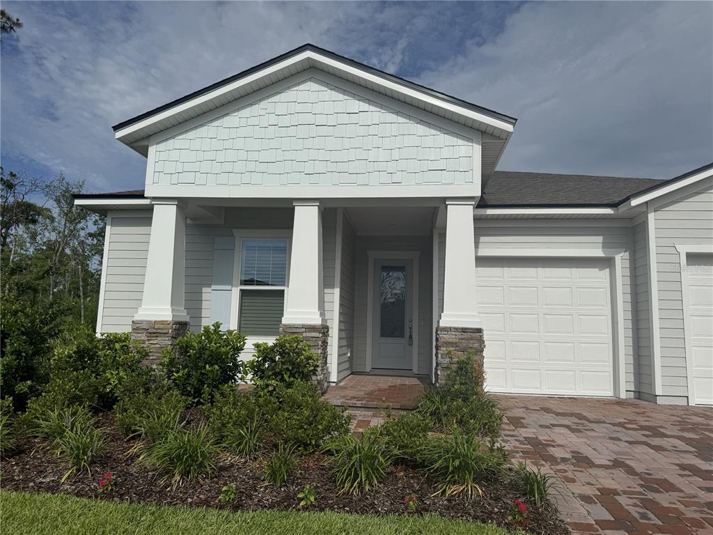 A single-story house exterior features light siding, stone-based columns, and a paved driveway — 6 BLUE GROTTO PLACE, PALM COAST, FL
