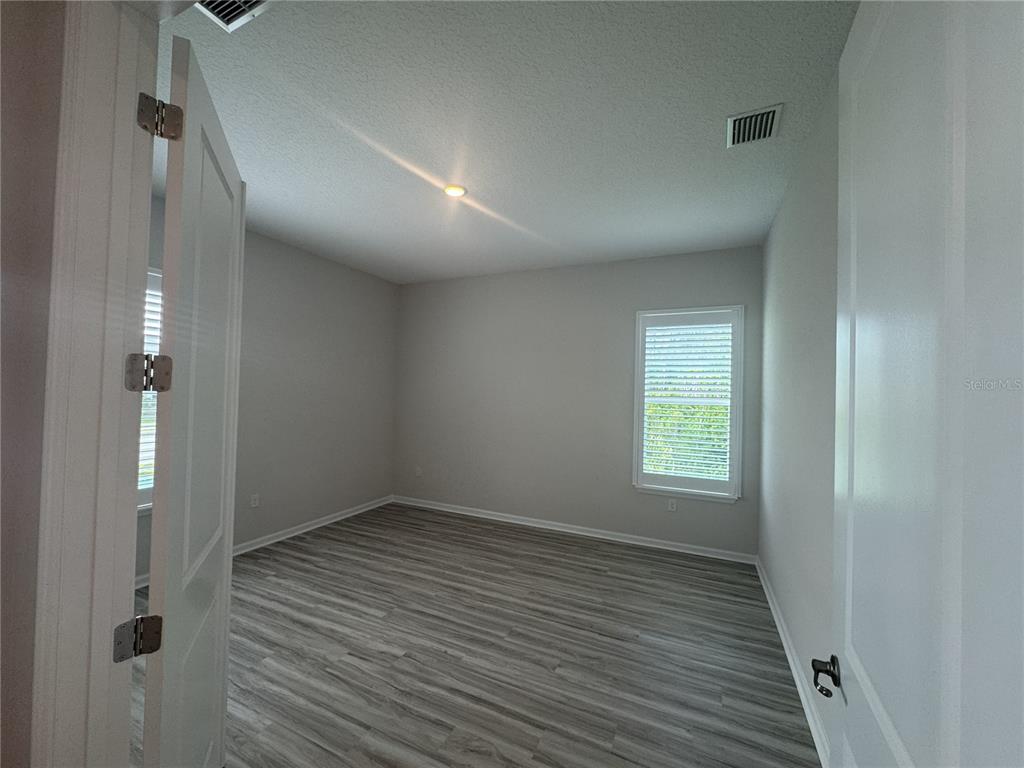 An empty room features light gray walls, wood-look flooring, a window with shutters, and recessed lighting — 6 BLUE GROTTO PLACE, PALM COAST, FL