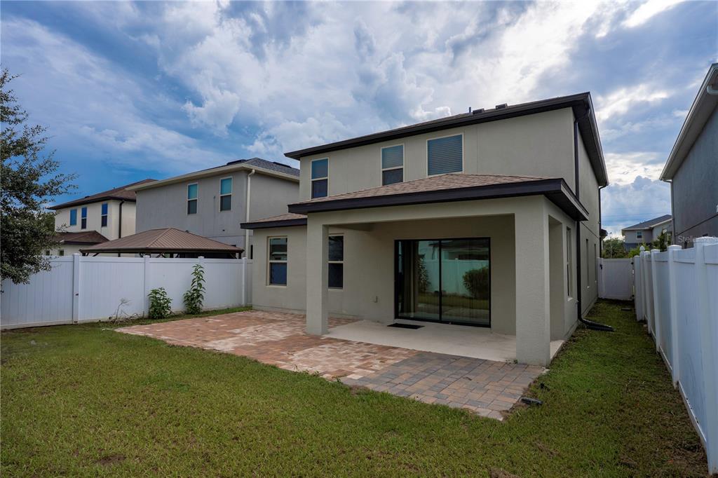 The exterior of a two-story house features a covered patio and a paved backyard area — 2905 SUMMER GREEN TRAIL, KISSIMMEE, FL