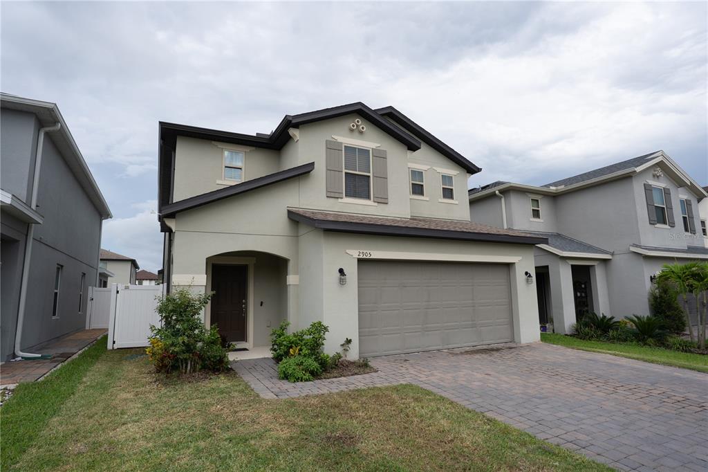 A two-story suburban house with a beige stucco exterior, a two-car garage, and a paver driveway — 2905 SUMMER GREEN TRAIL, KISSIMMEE, FL