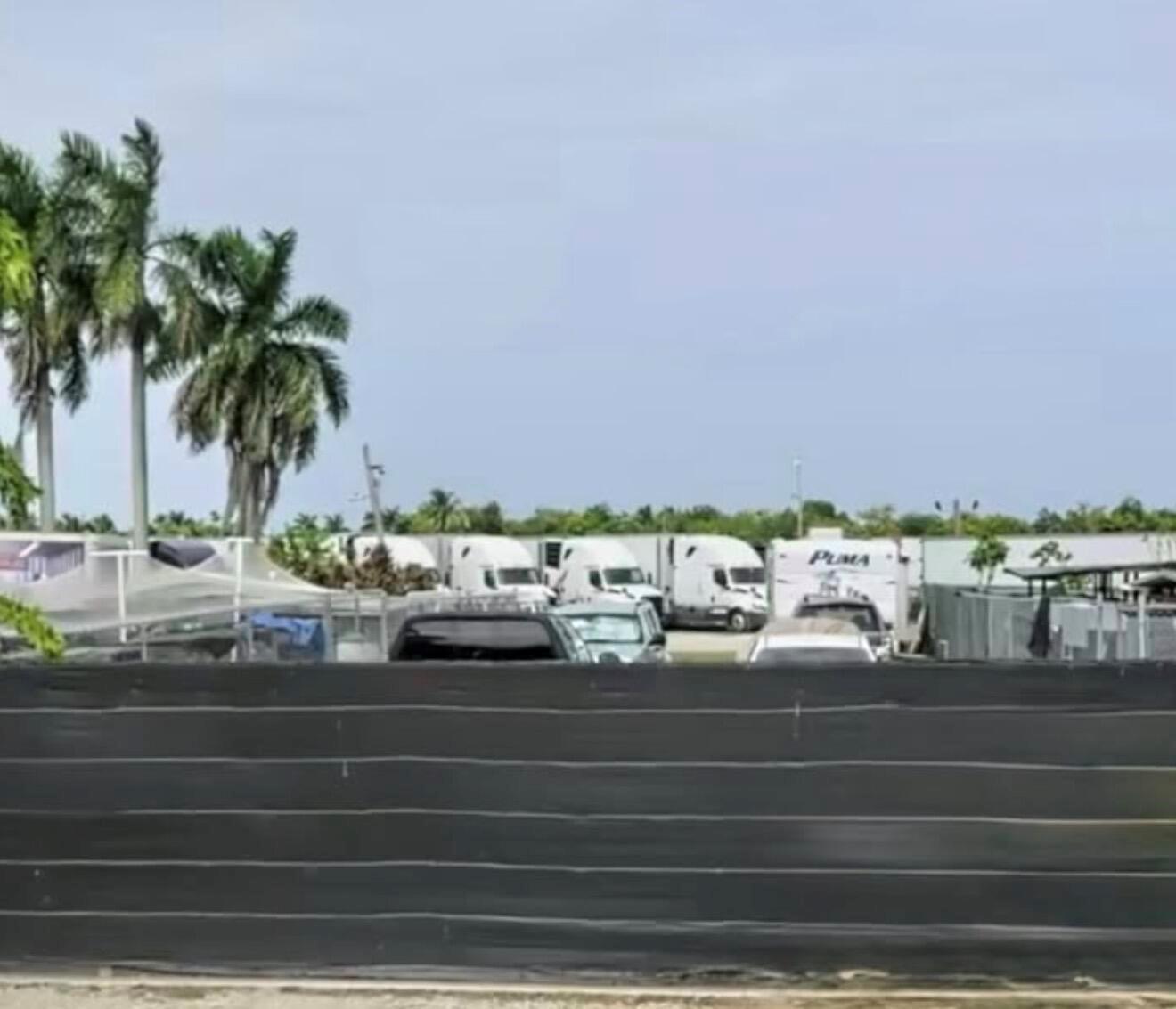 A view of a parking lot containing several semi-trucks and a trailer behind a fence — MIAMI, FL