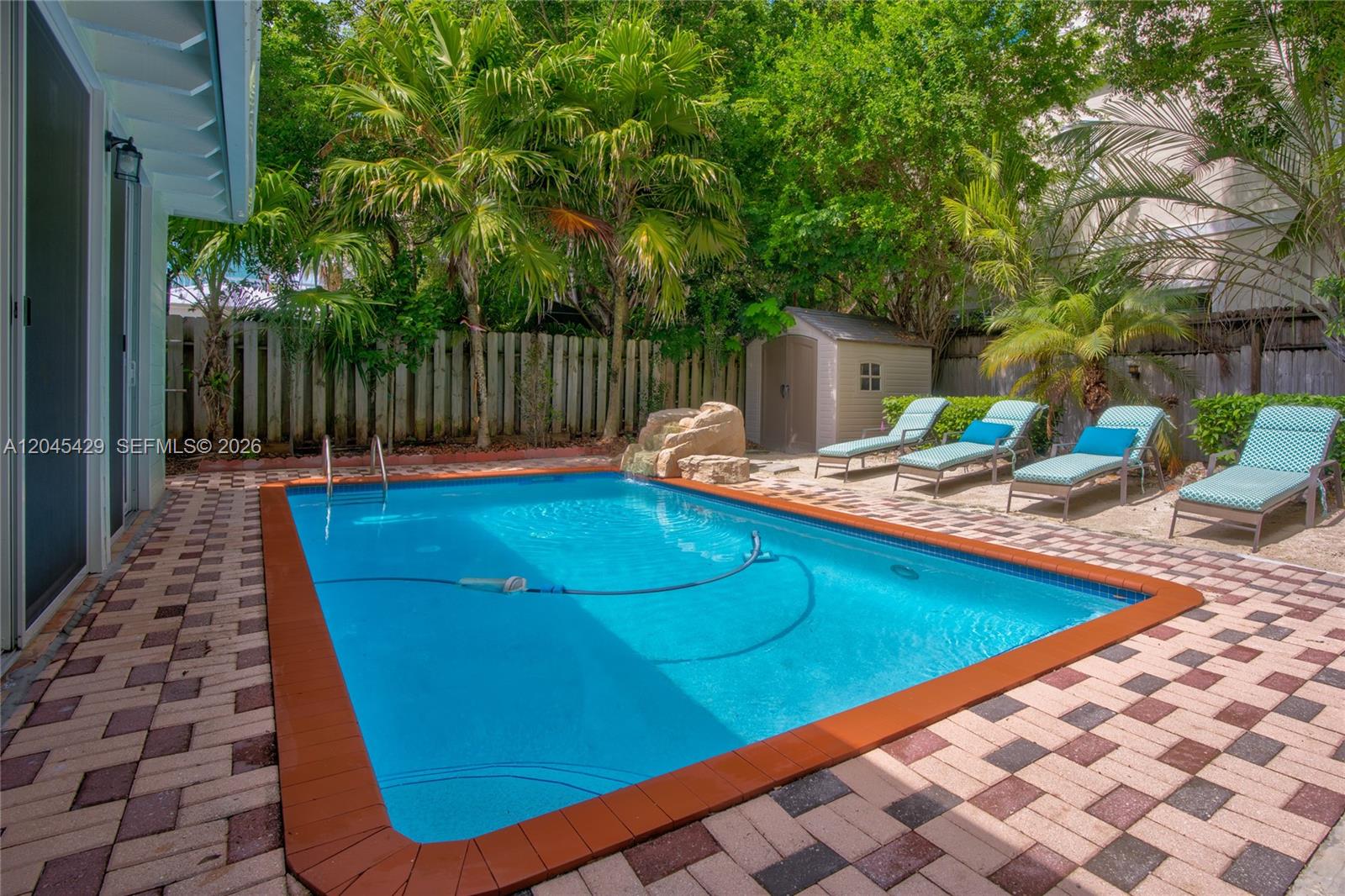 A rectangular swimming pool with a stone waterfall feature sits on a paved patio — 27 Blue Runner St, Key Largo FL 33037, KEY LARGO, FL