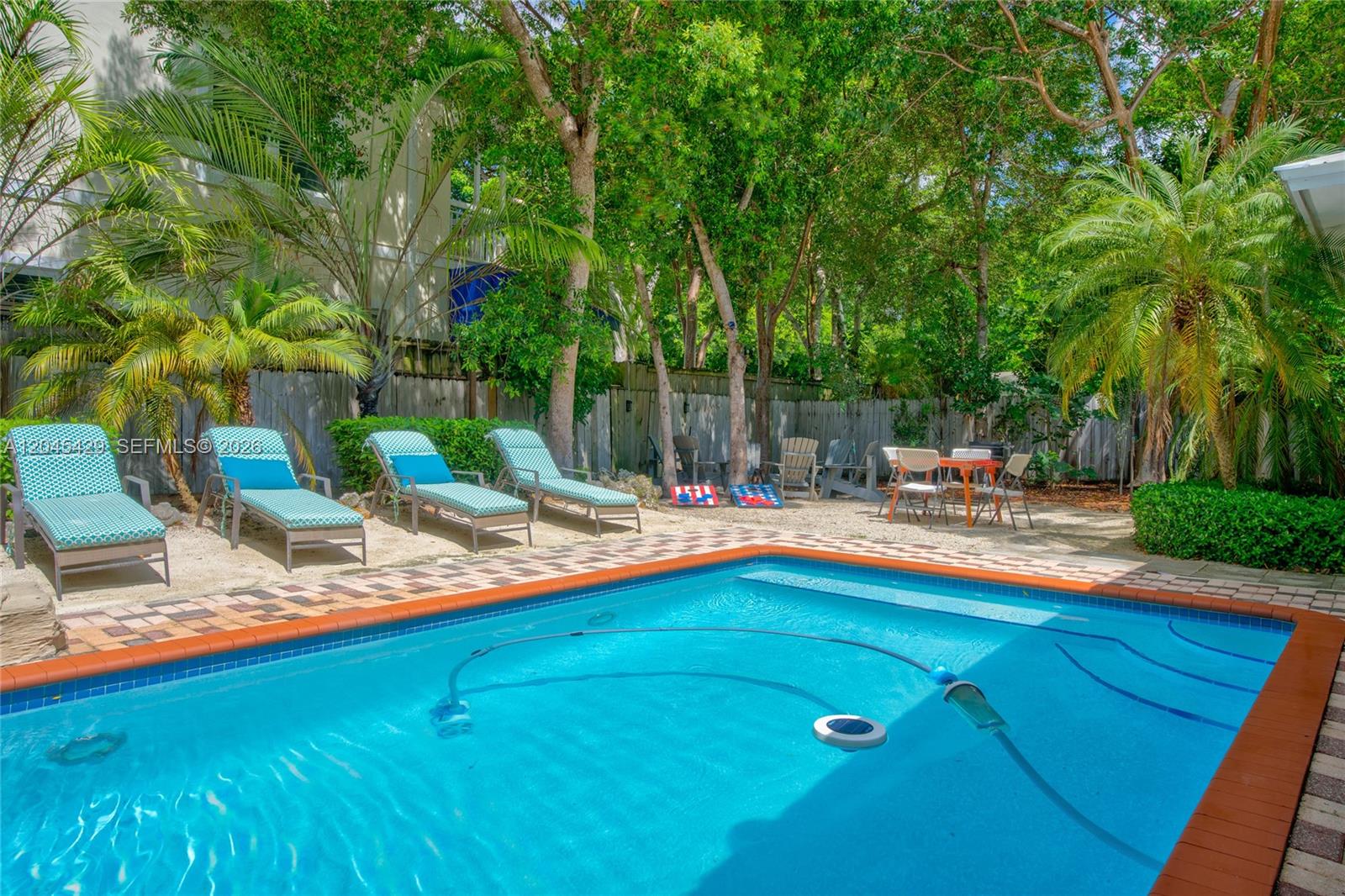 A swimming pool sits in front of a patio with lounge chairs and dining furniture — 27 Blue Runner St, Key Largo FL 33037, KEY LARGO, FL