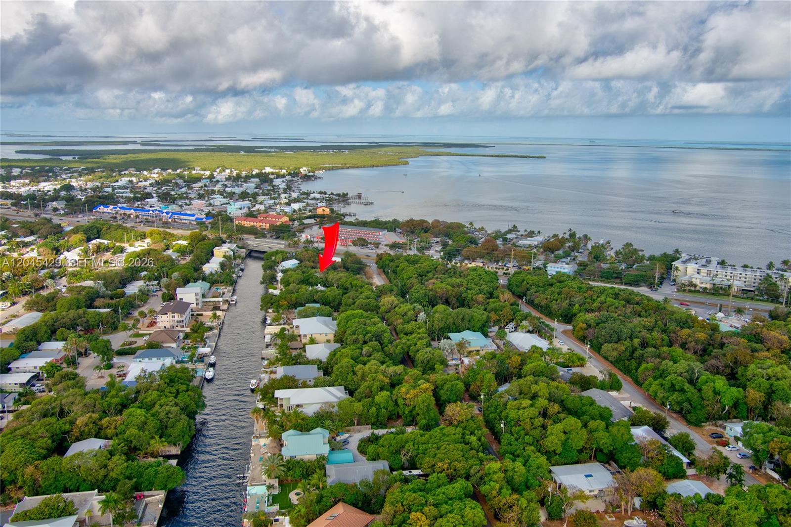 This aerial view shows a canal-front residential neighborhood surrounded by dense trees near water — 27 Blue Runner St, Key Largo FL 33037, KEY LARGO, FL